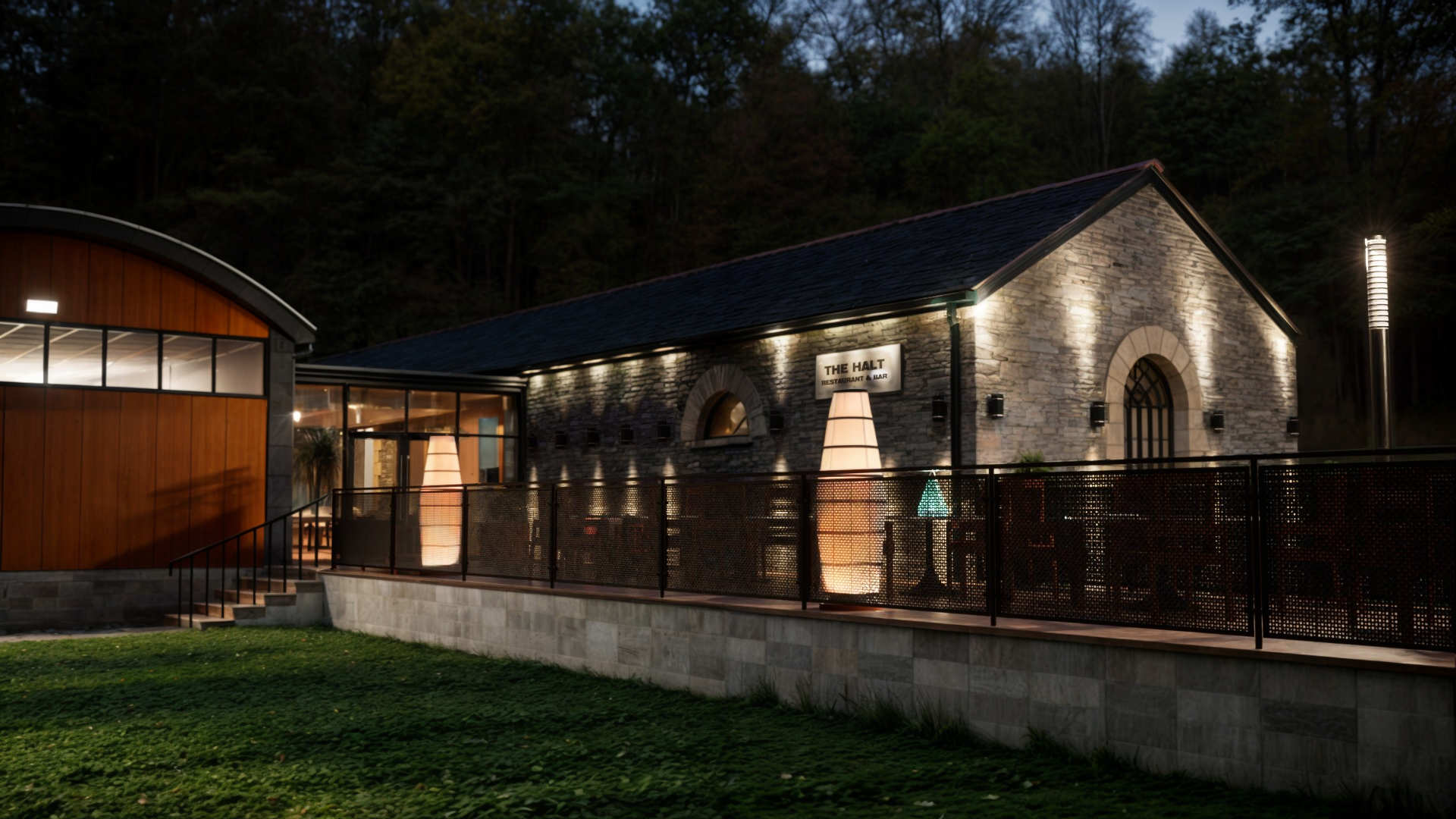 Restaurant & bar building in County Donegal designed by Usonia Architects, housed in a former railway building featuring an original stone facade, arched windows, complemented by a modern extension featuring a curved roof with coloured cladding panels, set amidst lush greenery and tall trees. Outdoor patio area with stylish fencing and planters.