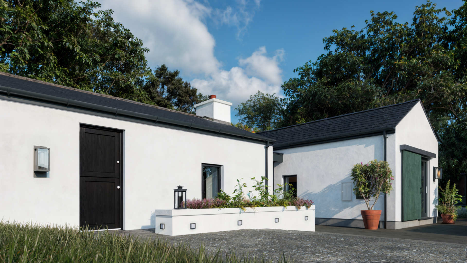 House Extension 6 Donegal Architect - Image19- Image shows an extension to a 19th century Donegal cottage featuring smooth white walls and slate roof and a large patio garden area. House is surrounded by trees and grass.